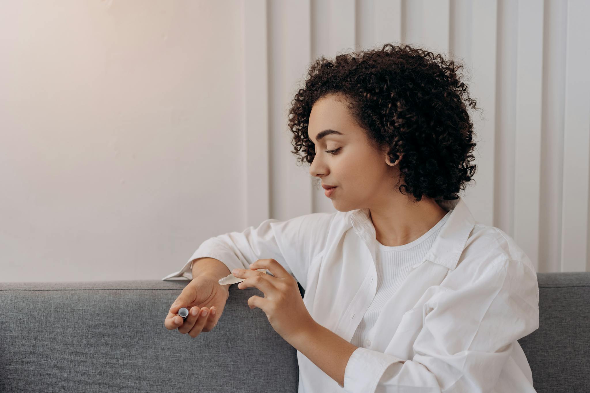 A young woman applies essential oil while relaxing indoors, promoting wellness and self-care in a calming environment.